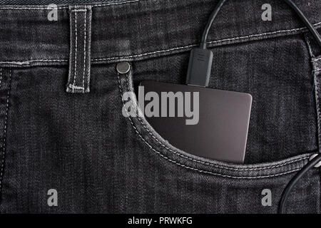 Disque dur portable noir avec câble dans le cas réside dans la poche avant du jean noir Banque D'Images