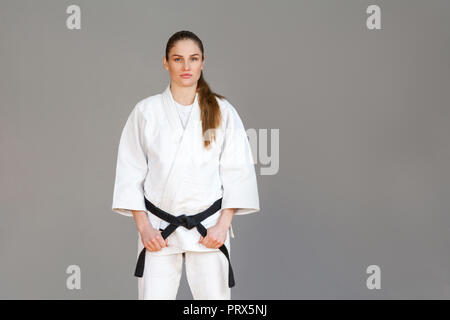 Belle jeune femme athlétique en kimono blanc debout et tenant la ceinture noire et à la recherche à l'appareil photo avec visage sérieux. Concept arts martiaux japonais. Banque D'Images