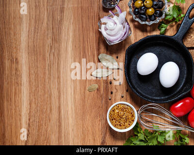 Sur un fond de bois horizontalement avec copyscera les oeufs de poulet dans une poêle en fonte, oignons, olives, tomates, verts, un batteur Banque D'Images