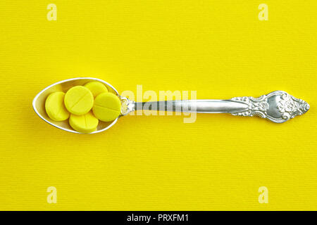 Cuillère en argent avec des pilules sur fond jaune. Banque D'Images