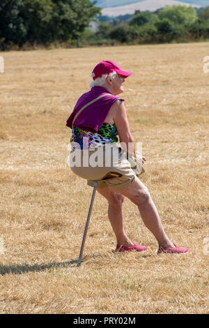 Un vieux ou vieille dame assise sur un stick de tir dans un champ vide. Banque D'Images