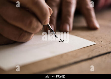 Personne à l'aide d'une plume et d'encre à faire la calligraphie dans une vue en gros plan de ses mains et la première lettre dessinée sur le papier. Banque D'Images
