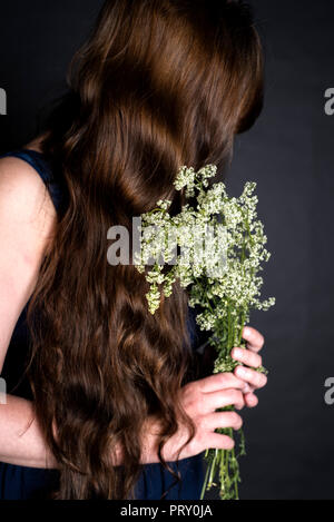 Un portrait d'une jeune femme avec un livre blanc, gratteron Galium mollugo Banque D'Images