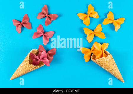 Mise en page d'été créative faite de cornet de crème glacée, cornets et gaufres pâtes de couleur papillon lumineux sur la semoule fond bleu clair. Concept minimal Banque D'Images