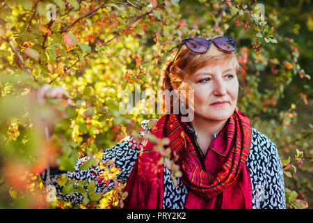 Femme d'âge moyen élégant posant en forêt d'automne. Senior lady portant des vêtements neufs et accessoires. Fashion outfit Banque D'Images