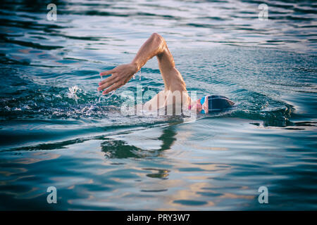 La respiration au cours de natation nageur ramper dans la mer au coucher du soleil Banque D'Images