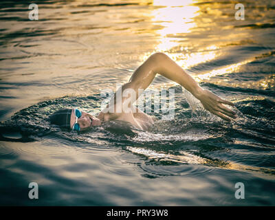 La respiration au cours de natation nageur ramper dans la mer au coucher du soleil Banque D'Images