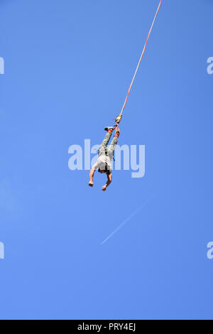 Le saut de crane pendant Sofia Sports extrêmes. L'homme suspendu à un cordon haut dans le ciel bleu. Sentier de l'avion blanc vu à distance au-dessous de lui Banque D'Images