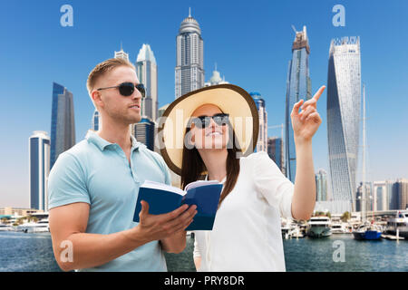 Smiling Young Woman Showing Direction à son mari Holding Guide Book en ville Banque D'Images