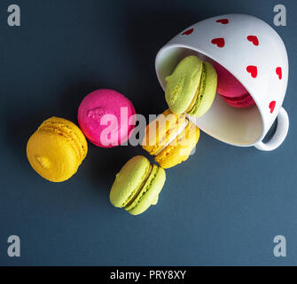 Les gâteaux ronds macarons multicolores ont abandonné d'une tasse en céramique blanche, fond noir, vue du dessus Banque D'Images