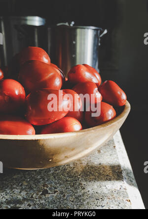 Bol en bois de tomates Roma sur comptoir en granit avec des ustensiles de cuisine en acier inoxydable, préparé pour la mise en conserve. Banque D'Images