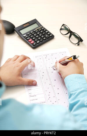 L'homme est de remplir la fiche de lecture OMR avec stylo. Photo de calculatrice, verres et de la souris sur la table. Banque D'Images