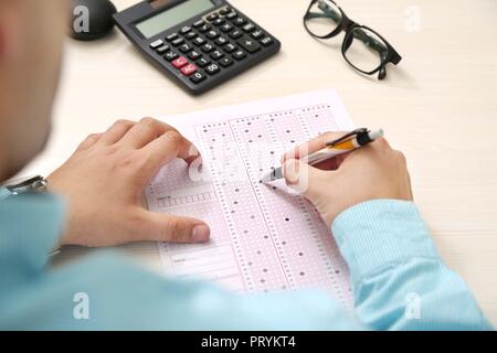 L'homme est de remplir la fiche de lecture OMR avec stylo. Photo de la calculatrice et les verres sur la table. Banque D'Images