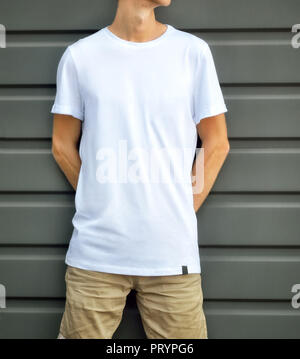 Simulateur de vêtements urbains. Jeune homme appuyé contre le mur texturé gris dans un T-shirt blanc et un short marron. Template design prêt pour vous. Banque D'Images