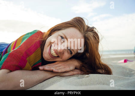 Femme rousse allongée dans le sable sur la plage, les yeux fermés Banque D'Images