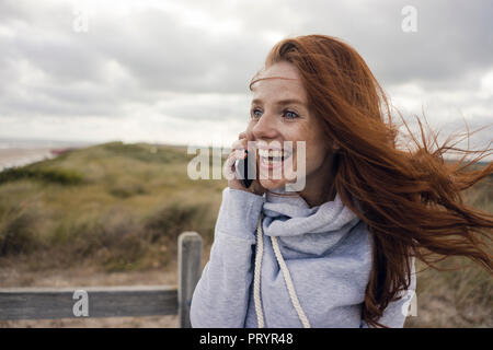 Femme rousse à l'aide du smartphone sur la plage Banque D'Images