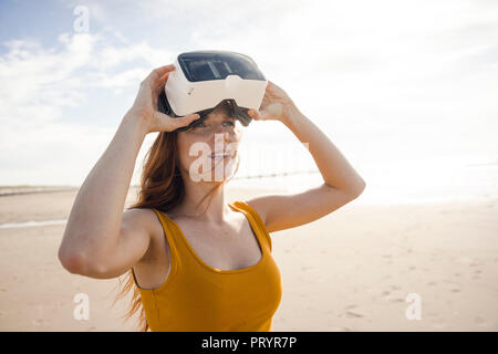 Femme rousse à l'aide de lunettes VR sur la plage Banque D'Images