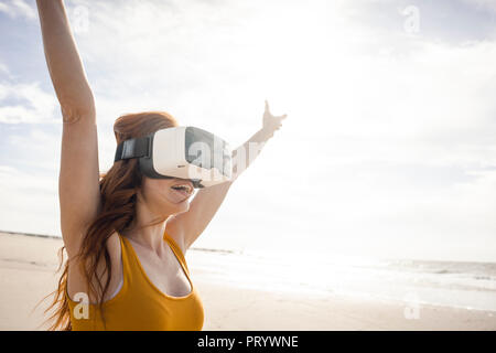 Femme rousse à l'aide de lunettes VR sur la plage Banque D'Images