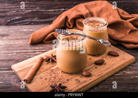 Dessert caramel caramel en pot, saupoudrée de chocolat râpé. Sur planche de bois, décoré avec des amandes et de la cannelle, l'anis étoilé. En bois rustique Banque D'Images