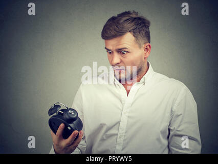 Jeune homme en chemise formelle à la recherche au réveil avec la peur d'être en retard sur fond gris Banque D'Images