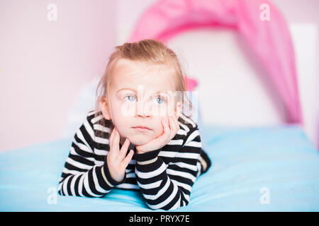 Portrait de la rêverie little girl lying on bed at home Banque D'Images