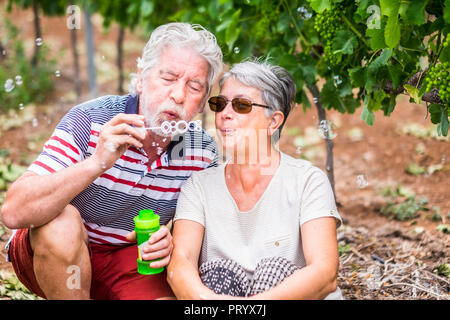 Belle caucasian couple senior homme et femme faire des bulles de savon ensemble pour jouer et s'amuser avec joie, heureux de l'emplacement en plein air dans la nature des activités de loisirs Banque D'Images
