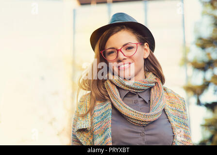 Charmante femme moderne wearing hat avec des lunettes et foulard looking at camera in sunlight Banque D'Images