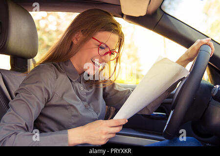 Vue latérale du jeune femme dans les verres de papier avec les résultats du test de lecture tout en restant assis dans la voiture et souriant joyeusement Banque D'Images