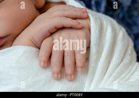 Close-up of little baby poignées. Le nouveau-né garçon dormir sous une couverture en tricot blanc bleu se trouve sur la fourrure. Banque D'Images