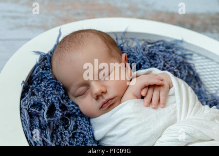 Petit bébé garçon endormi dans un panier sur le plancher en bois, studio shot Banque D'Images