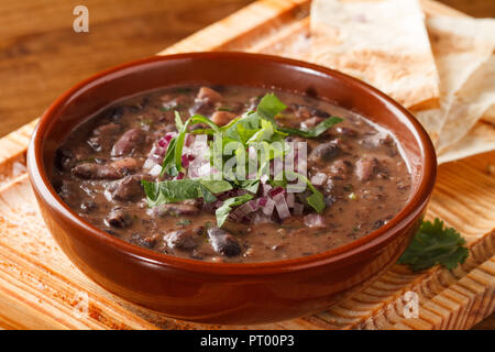 Soupe de haricots rouges, servie sur une planche en bois avec des morceaux de pain. Banque D'Images