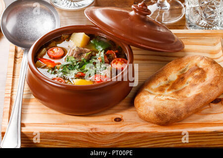 Le Khachlama est un ragoût d'agneau arménien traditionnel composé de pommes de terre, de poivre et de tomates, servi dans une casserole d'argile avec du pain sur une planche de bois. Banque D'Images