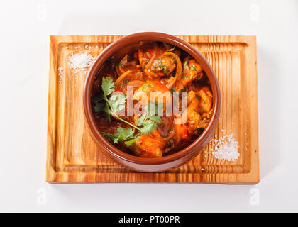 Curry de poulet servi dans un pot/bol en argile servi sur un panneau de bois, isolé dans un fond blanc. Banque D'Images