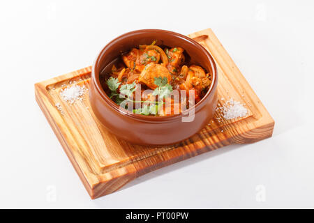 Curry de poulet servi dans un pot/bol en argile servi sur un panneau de bois, isolé dans un fond blanc. Banque D'Images