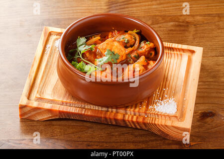 Curry de poulet servi dans un pot/bol en argile sur une planche de bois. Banque D'Images