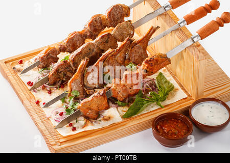 Khorovats- Kebab arménien traditionnel / plateau de brochettes sur bois. Brochettes de veau, d'agneau, de porc et de poulet servies sur du pain plat sur fond blanc. Banque D'Images