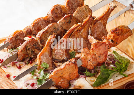 Khorovats- Kebab arménien traditionnel / plateau de brochettes sur bois. Brochettes de veau, d'agneau, de porc et de poulet servies sur du pain plat sur fond blanc. Banque D'Images