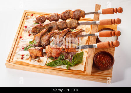 Khorovats- Kebab arménien traditionnel / plateau de brochettes sur bois. Brochettes de veau, d'agneau, de porc et de poulet servies sur du pain plat sur fond blanc. Banque D'Images