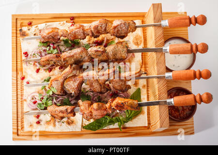 Khorovats- Kebab arménien traditionnel / plateau de brochettes sur bois. Brochettes de veau, d'agneau, de porc et de poulet servies sur du pain plat sur fond blanc. Banque D'Images