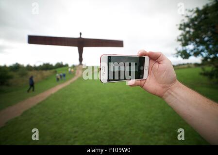 Prenant une photo touristique de l'Ange de la statue du Nord avec leur téléphone portable, une personne photographiant l'Ange de la sculpture du Nord dans le comté de Tyne et Wear. Banque D'Images