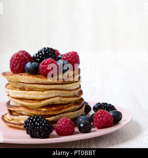 Crêpes aux fruits rouges sur une plaque en bois blanc, rose sur la surface, close-up. Vue de côté. Banque D'Images