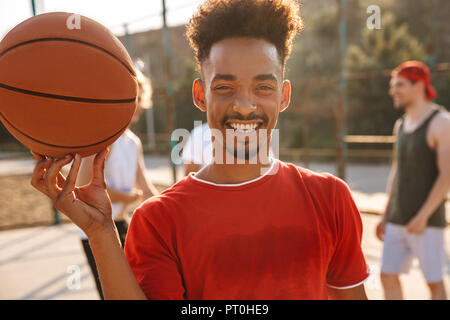 Portrait of american guy bille sur son doigt tout en jouant au basketball à l'aire de jeux Piscine en plein air avec ses amis Banque D'Images