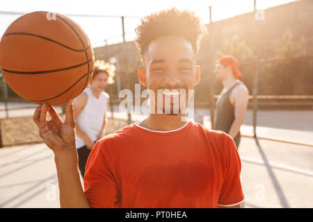 Image de jeune garçon sportif bille sur son doigt tout en jouant au basketball à l'aire de jeux Piscine en plein air avec son équipe Banque D'Images