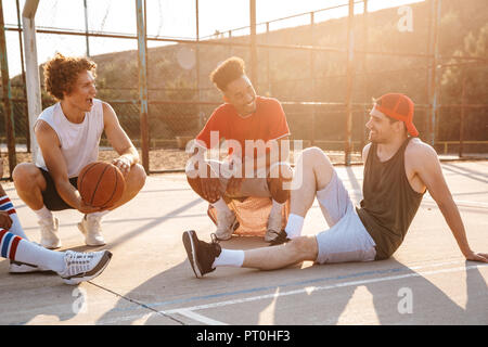 Groupe de joyeux amis multiethnique de joueurs de basket-ball assis au terrain de sport Banque D'Images