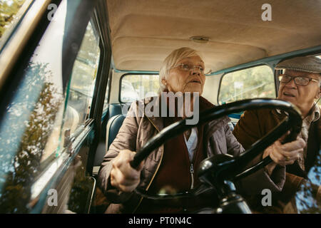 Vieille Femme au volant d'une voiture et de parler avec son mari assis dans le siège passager. Vieux couple roulant en voiture d'époque. Banque D'Images