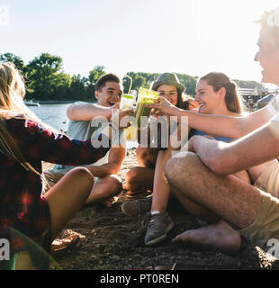 Groupe d'amis heureux assis au bord du fleuve le grillage avec boissons Banque D'Images
