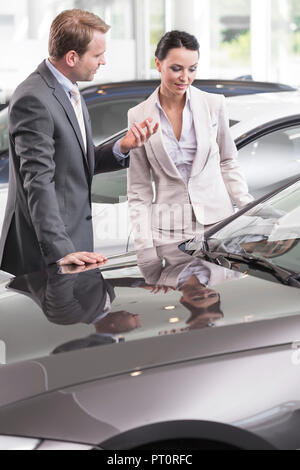 Au concessionnaire, vendeur montrant nouvelle voiture au client Banque D'Images