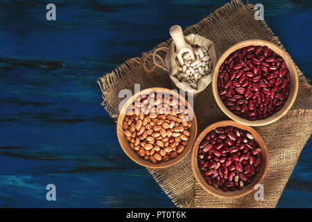 Assortiment de plats en bois dans les haricots et les haricots blancs dans un sac de lin bleu foncé sur fond de bois, de haricot mungo, haricot rouge, haricot blanc Banque D'Images