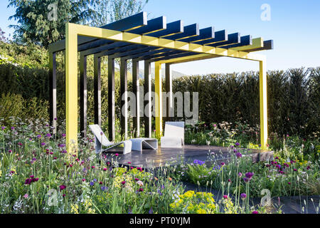 Pergola à cadre en acier avec toit en bois peint, terrasse en bois sombre, table de salon contemporaine, plantation de style prairie Allium hollandicum Spring UK Banque D'Images