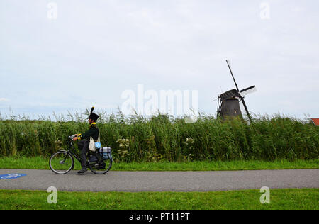 Homme dans un costume traditionnel équitation son vélo le long du chemin à travers le patrimoine de Kinderdijk, Pays-Bas Banque D'Images